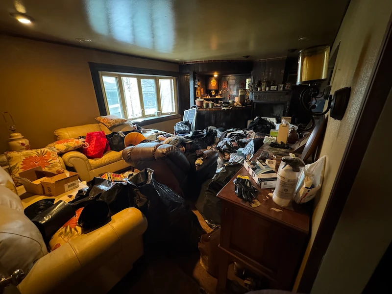 A very cluttered family room in Milltown, North Jersey filled with black trash bags and old furniture before an estate cleanout by JunkDoctors.