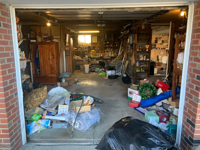 An overwhelmed residential garage packed with household debris, cardboard, holiday decorations, and trash bags requiring professional junk hauling services in Hasbrouck Heights, New Jersey.