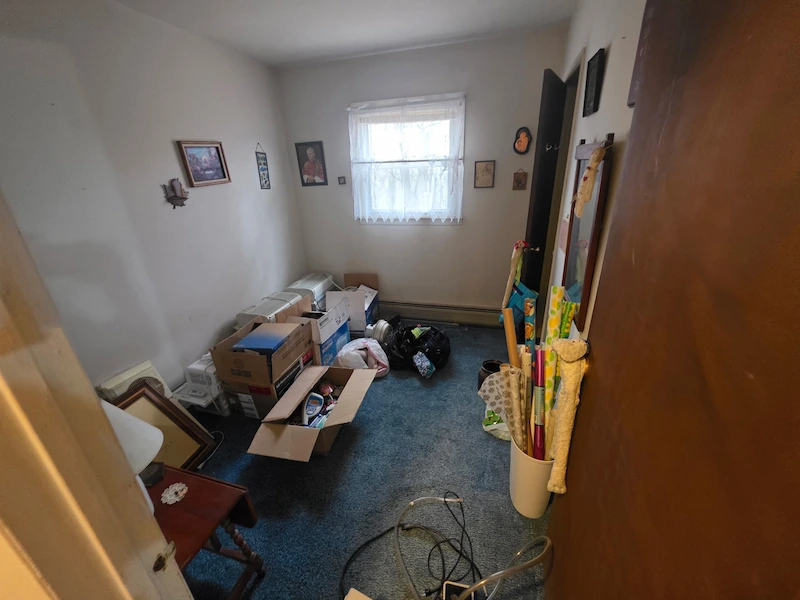 Before photo of a small room used for storage, filled with cardboard boxes and miscellaneous household junk in Secaucus, New Jersey.