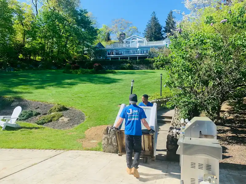 Junk Doctors NJ crew members carefully moving an old refrigerator down patio steps for removal and disposal.