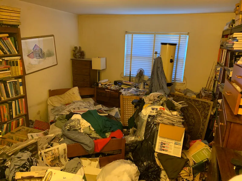 A bedroom in Hackettstown, New Jersey with heavy clutter, paper accumulation, and boxes before a selective hoarding cleanout.