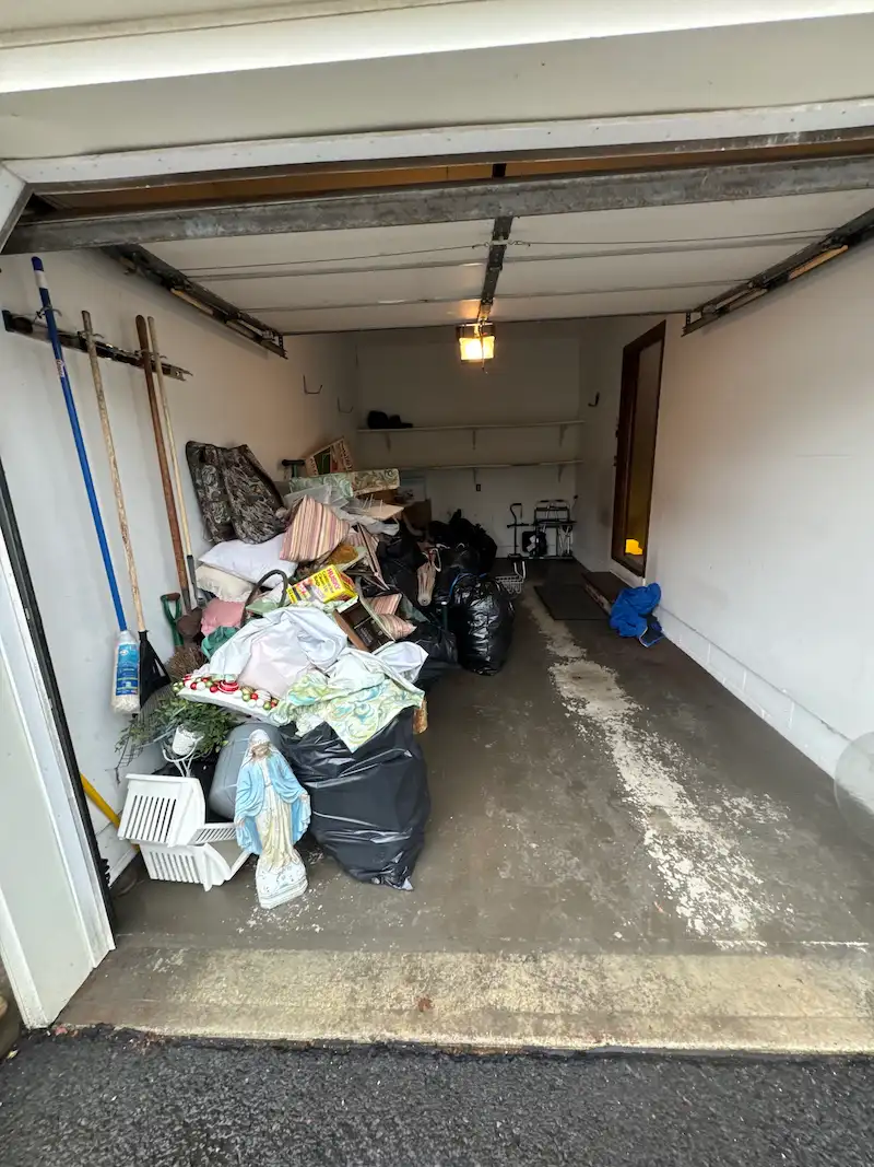 A suburban North Jersey garage filled with a large pile of black trash bags, old pillows, and miscellaneous household items before a Junk Doctors cleanout.